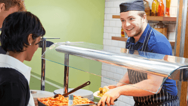 Personalausgabe in einer Kantine, mehrere Personen stehen in der Warteschlange.