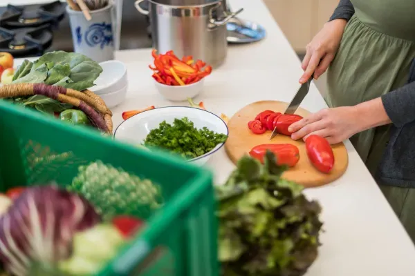 Person schneidet rote Paprika auf einem Schneidebrett in einer Küche mit frischem Gemüse