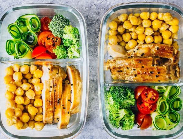 Zwei Glas-Lunchboxen mit Kichererbsen, gegrilltem Hähnchen, Brokkoli, Tomaten und Gurkenscheiben