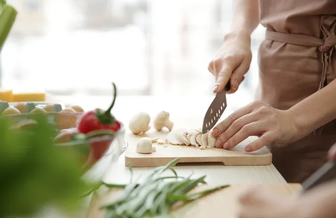 Person schneidet frische Champignons auf einem Holzbrett in einer hellen Küche