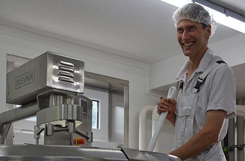 Lächelnder Mann in Arbeitskleidung neben industrieller Lebensmittelmaschine in Produktionsraum