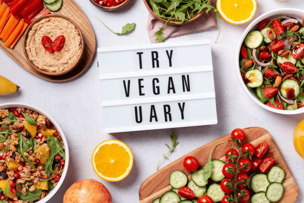 Tafel mit Aufschrift Try Vegan Uary umgeben von bunten veganen Gerichten und frischem Gemüse