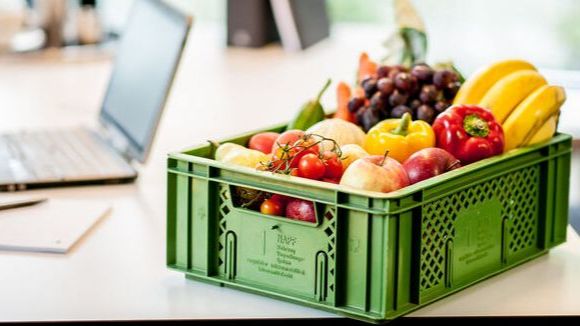 Kiste mit frischem Obst auf Bürotisch neben Laptop