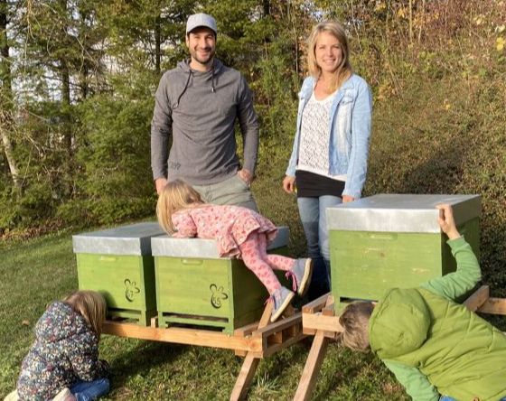 Familie mit Kindern erforscht grüne Bienenstöcke im Garten an sonnigem Tag