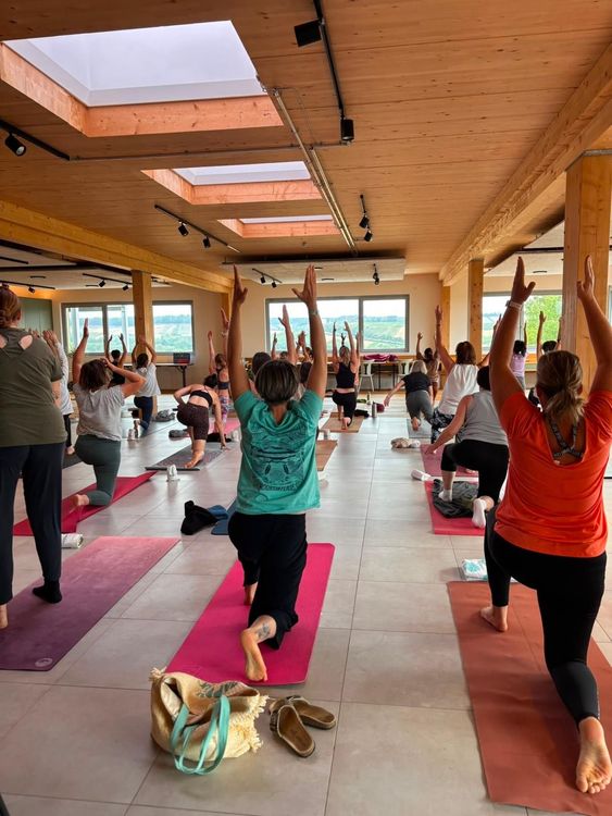 Menschen praktizieren Yoga in einem hellen Raum mit Holzbalken und großen Fenstern