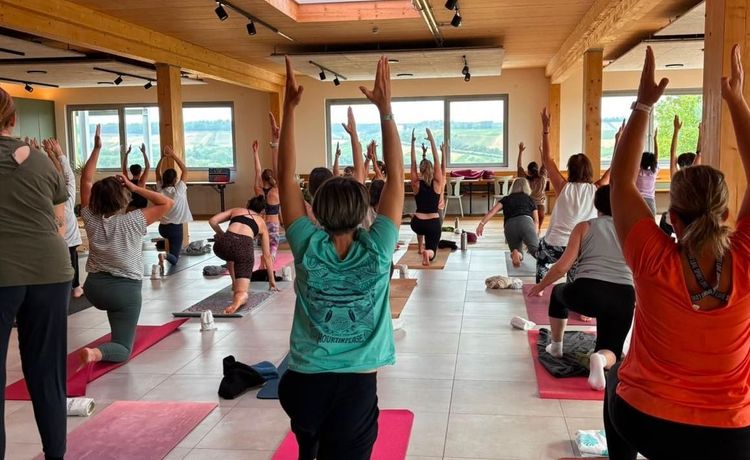 Gruppe von Menschen praktiziert Yoga in einem hellen Raum mit großen Fenstern und Holzdecke