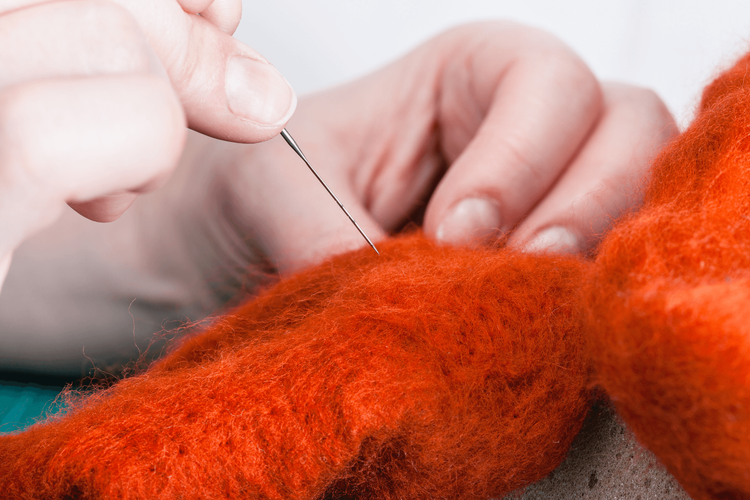 Nahaufnahme einer Hand, die mit einer Nadel roten Wollstoff bearbeitet