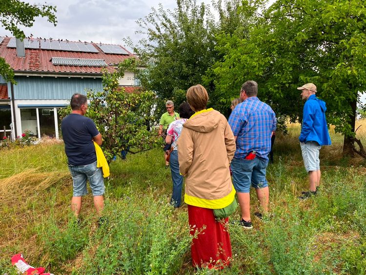 Gruppe von Menschen hört einem Mann im Garten mit Bäumen und Solarpanels auf Hausdach zu