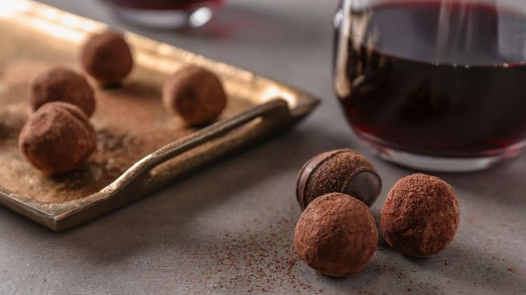 Schokoladentrüffel mit Kakaopulver auf Tisch neben Glas Rotwein und goldener Platte