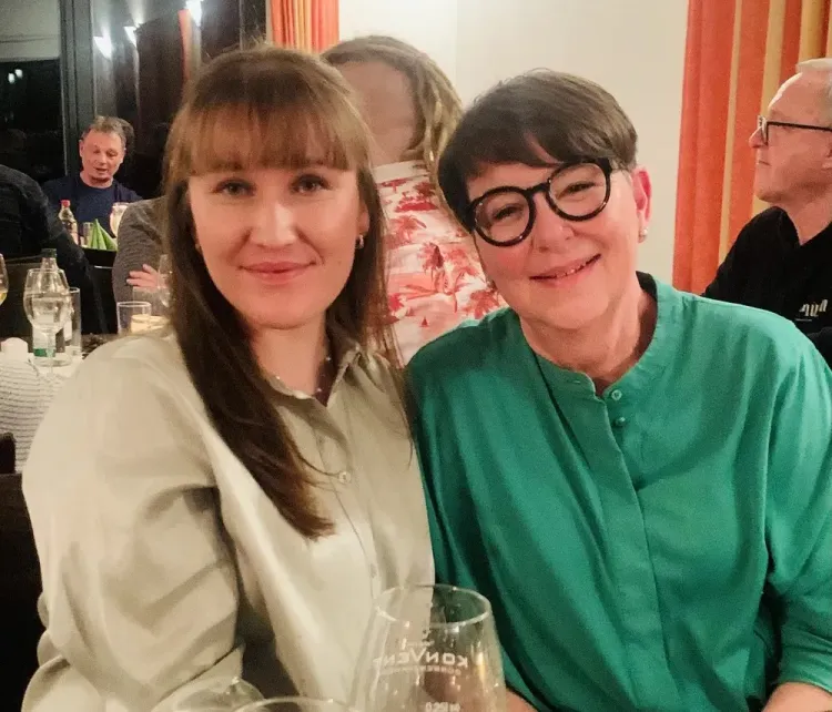 Zwei lächelnde Frauen sitzen in einem Restaurant bei einem geselligen Abend mit Getränken.