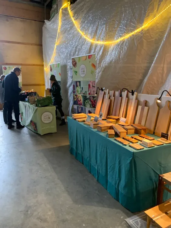 Marktstand mit Holzprodukten und Bio-Lebensmitteln in einer Halle mit gelber Beleuchtung