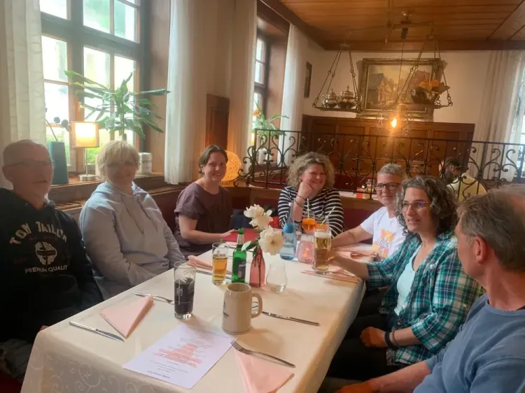 Sieben Personen sitzen an einem gedeckten Tisch in einem gemütlichen Restaurant mit warmem Licht.