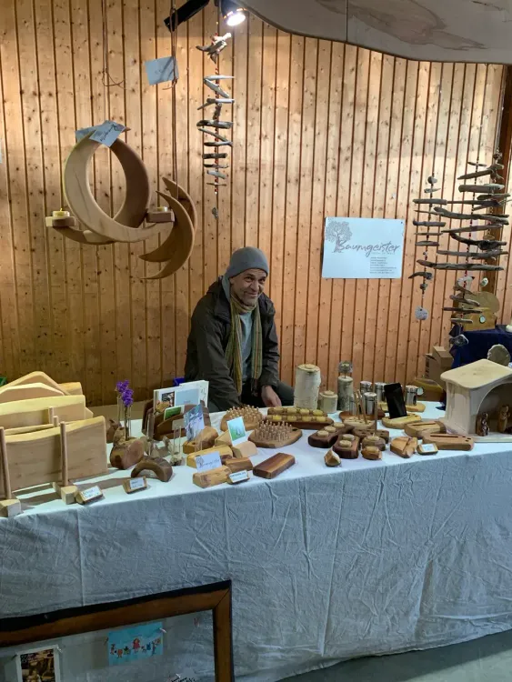 Verkäufer an einem Stand mit handgefertigten Holzkunstwerken vor Holzpaneelwand