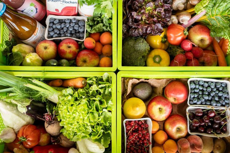 Vier grüne Kisten gefüllt mit frischem Obst und Gemüse wie Äpfeln, Blaubeeren, Salat und Karotten
