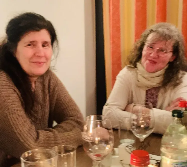 Zwei Frauen sitzen an einem Tisch mit Getränken und lächeln gesellig
