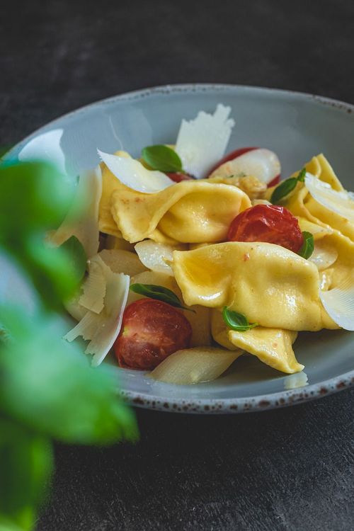Teller mit Tortellini, Kirschtomaten, Basilikumblättern und Parmesanspänen