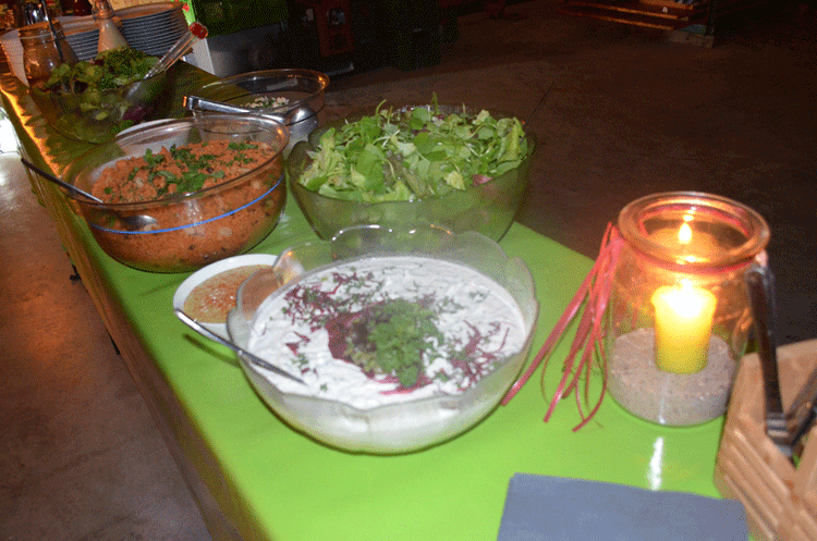 Verschiedene Salate und Dips in Glasschüsseln auf grünem Tisch mit brennender Kerze im Glas