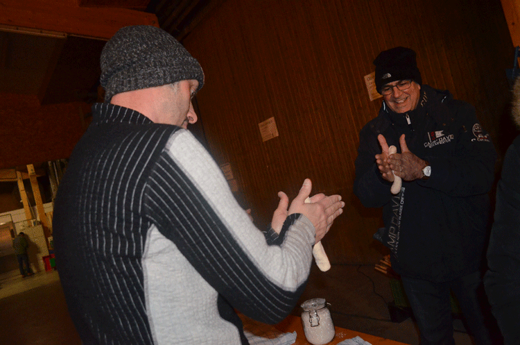 Zwei Männer formen Teigstücke in einer Holzhütte bei einer gemeinschaftlichen Aktivität