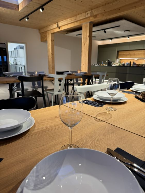 Moderner Esstisch mit weißem Geschirr und Weingläsern in einem Restaurant mit Holzdecke und Stühlen