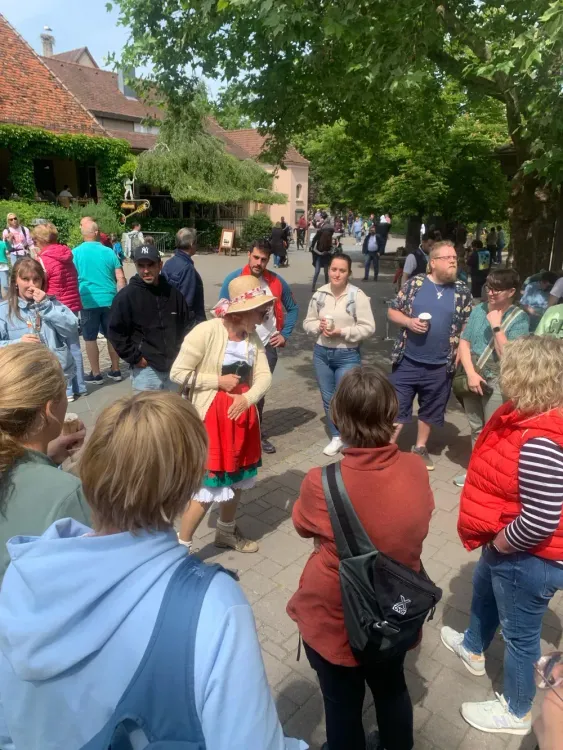 Menschen versammeln sich im Freien bei sonnigem Wetter vor traditionellen Gebäuden und Bäumen