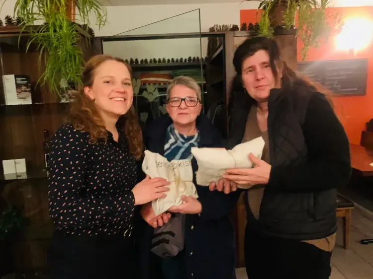 Drei Frauen in Innenraum halten verpackte Geschenke und lächeln in die Kamera