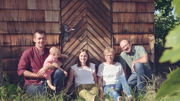 Fünfköpfige Familie sitzt vor einer Holzhaustür im Gras an einem sonnigen Tag