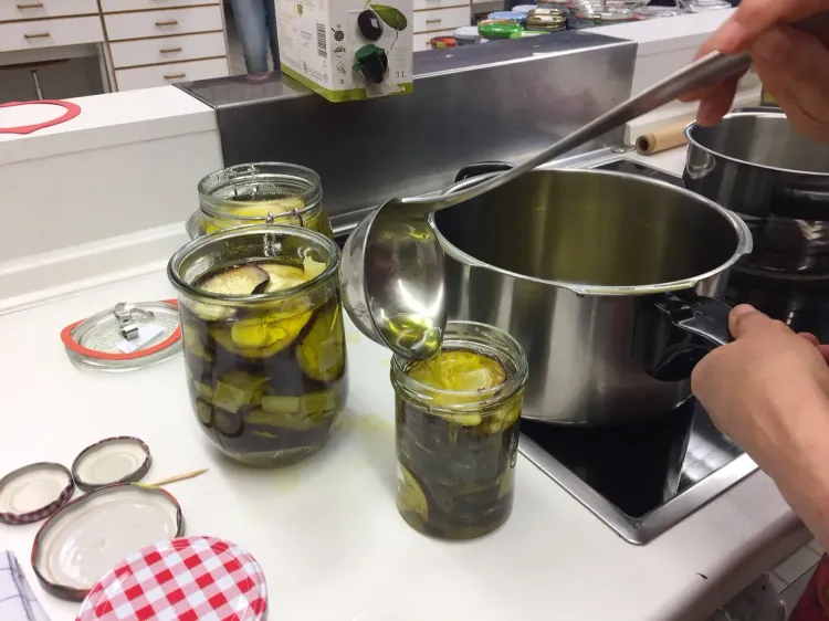 Öl wird mit Schöpfkelle in Einmachgläser mit Auberginenscheiben gegossen