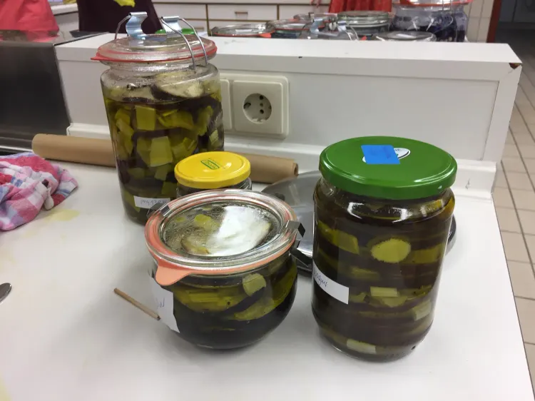 Vier Einmachgläser mit eingelegten Gemüsestücken auf einer weißen Küchenarbeitsplatte