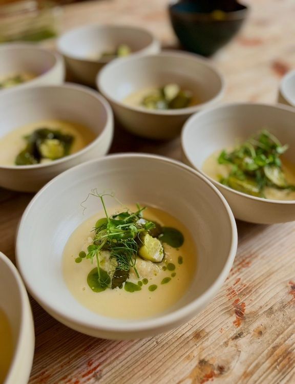 Mehrere weiße Schalen mit cremiger Suppe und grünen Kräutern auf rustikalem Holztisch