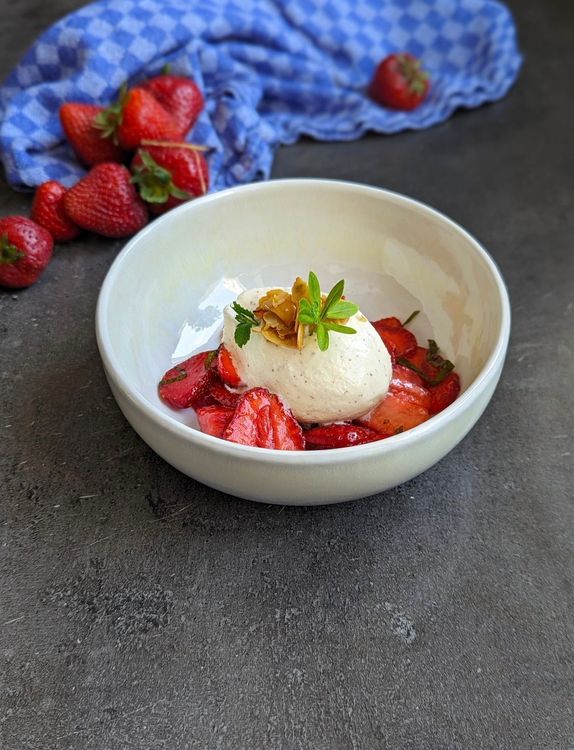 Schüssel mit Vanilleeis und frischen Erdbeeren auf grauem Untergrund mit blau kariertem Tuch