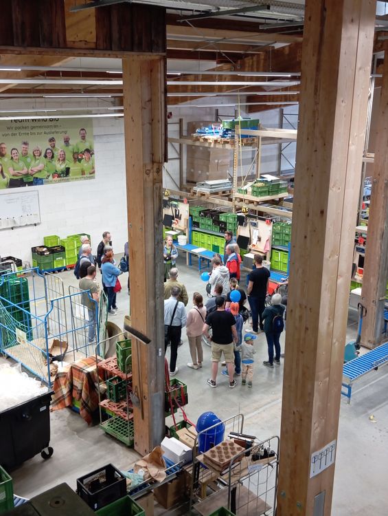 Menschen in einer Lagerhalle mit Holzstützen und grünen Kisten bei einer Führung