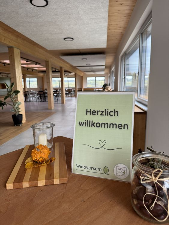 Ein Schild mit der Aufschrift Herzlich willkommen in einem hellen, modernen Raum mit Holzelementen und großen Fenstern