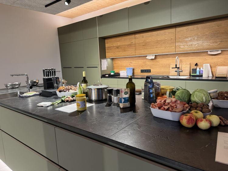 Moderne Küche mit grünem Schrank, Holzfronten und vielfältigen frischen Zutaten auf schwarzer Arbeitsplatte