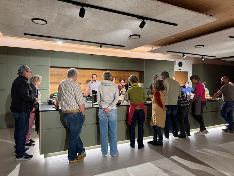 Gruppe von Menschen steht an einer modernen Kücheninsel und hört einem Mann beim Kochen zu