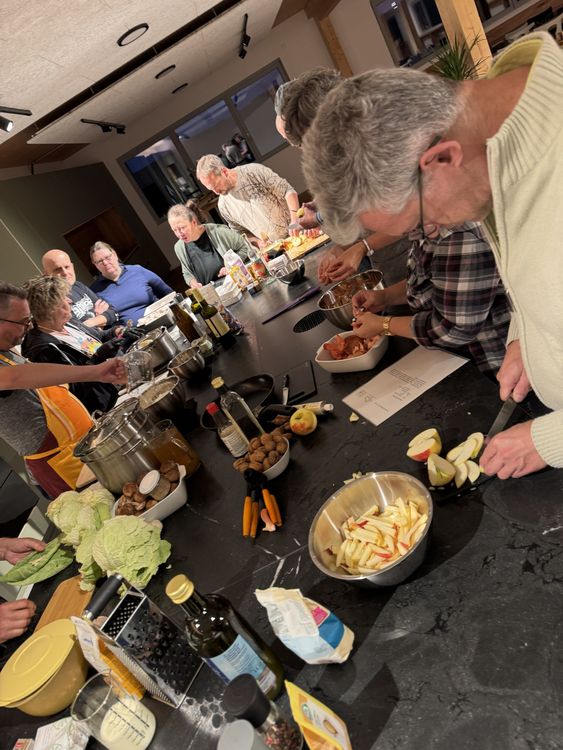 Gruppe von Erwachsenen bereitet gemeinsam in moderner Küche verschiedene Zutaten fürs Kochen vor.