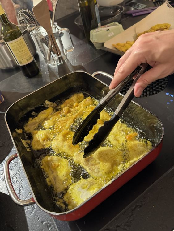 Frittieren von paniertem Essen in einer rechteckigen Pfanne mit einer Zange in der Hand