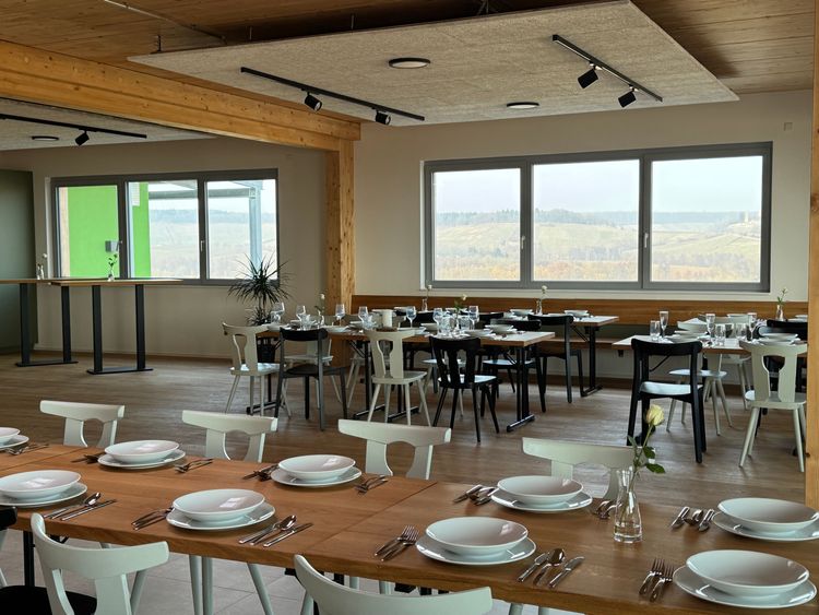 Modernes Restaurant mit Holztischen und weißen Stühlen, gedeckt mit Tellern, Besteck und Gläsern, großer Fensterblick auf Landschaft