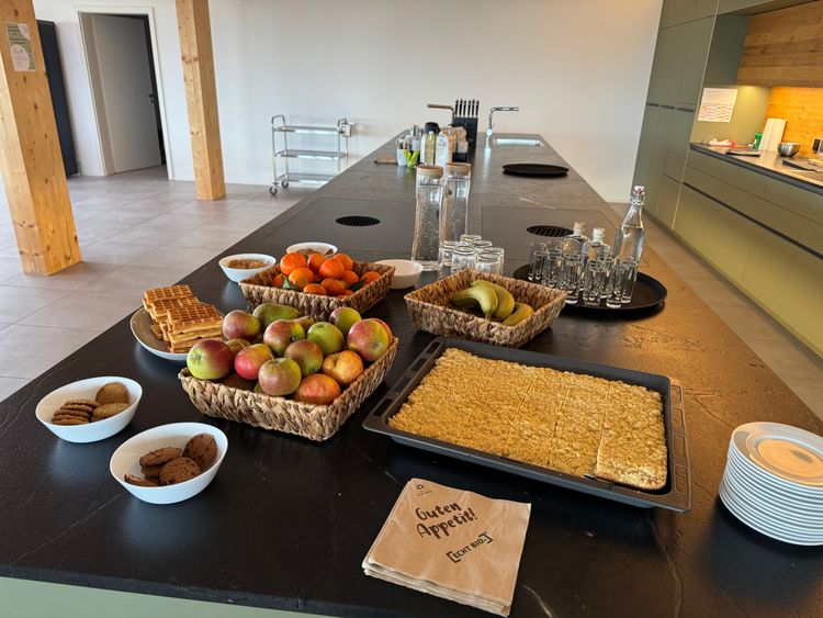 Großer Tisch mit Obstkörben, Waffeln, Keksen, Getränkeflaschen und Tellern in einer modernen Küche