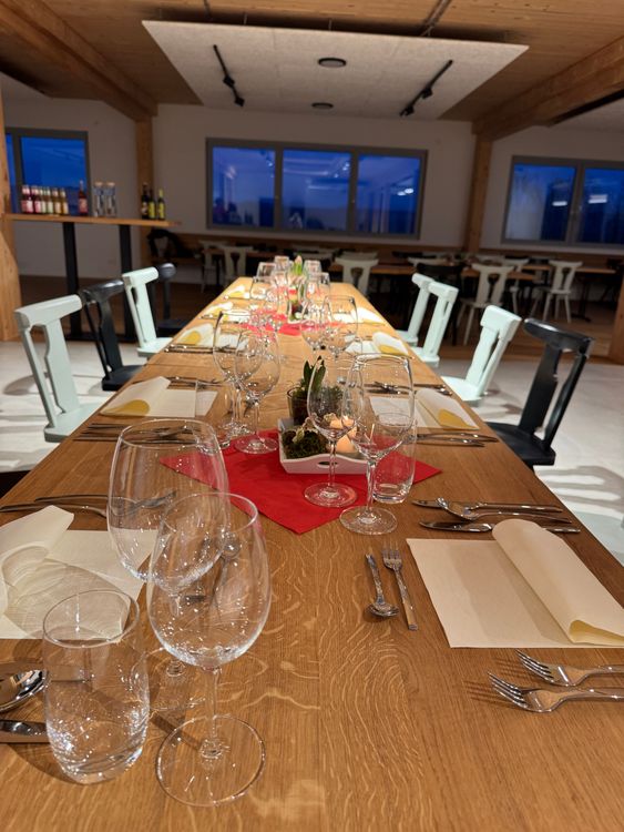 Langer, gedeckter Holztisch mit Weingläsern und Besteck in modernem Gastraum am Abend