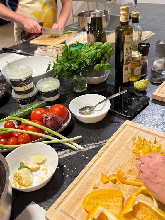 Personen schneiden Gemüse und frische Kräuter auf einer Küchenarbeitsplatte mit Zutaten und Gewürzen