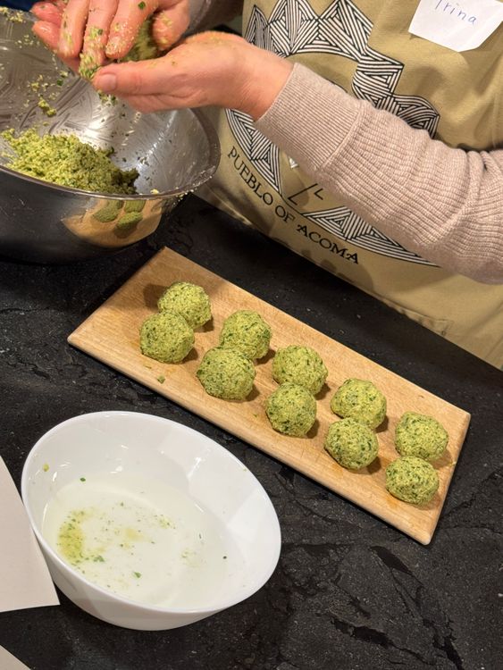 Hände formen grüne Falafelbällchen neben einer Schüssel und einem Holzbrett mit Falafel