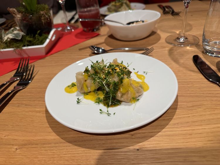 Teller mit gedämpften Dumplings, garniert mit Kräutern und gelber Sauce auf Holztisch.