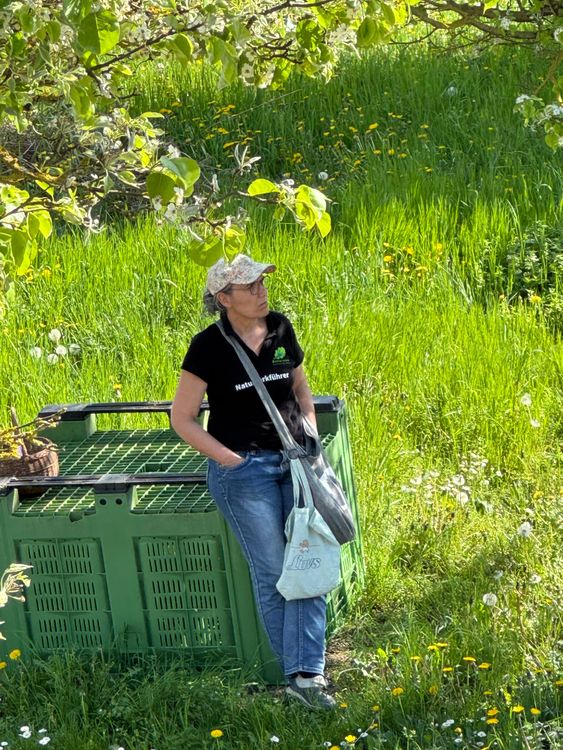 Frau lehnt an grüner Kiste im blühenden Gras unter Baum mit Hand in Tasche