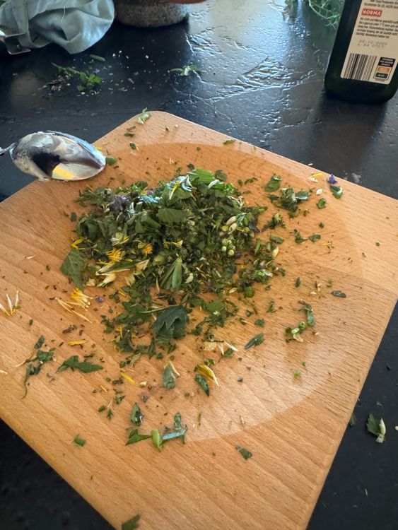 Holzschneidebrett mit gehackten frischen Kräutern und einem silbernen Löffel darauf