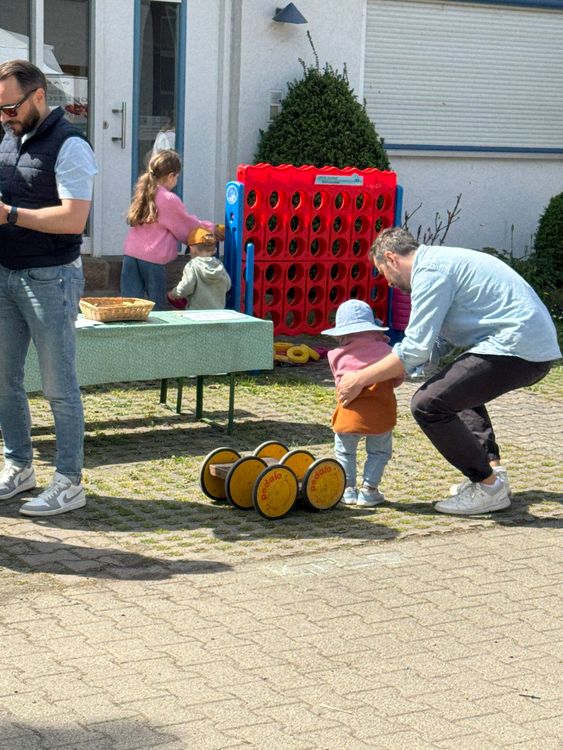 Vater hilft Kleinkind, während andere Kinder vor einem großen roten Spiel-4-gewinnt-Brett spielen