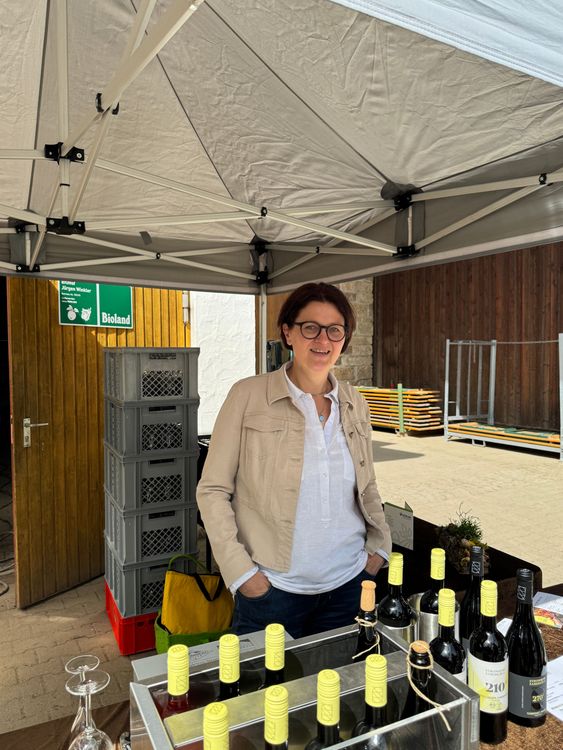 Frau steht unter Zelt an Tisch mit Weinflaschen bei Marktstand im Freien