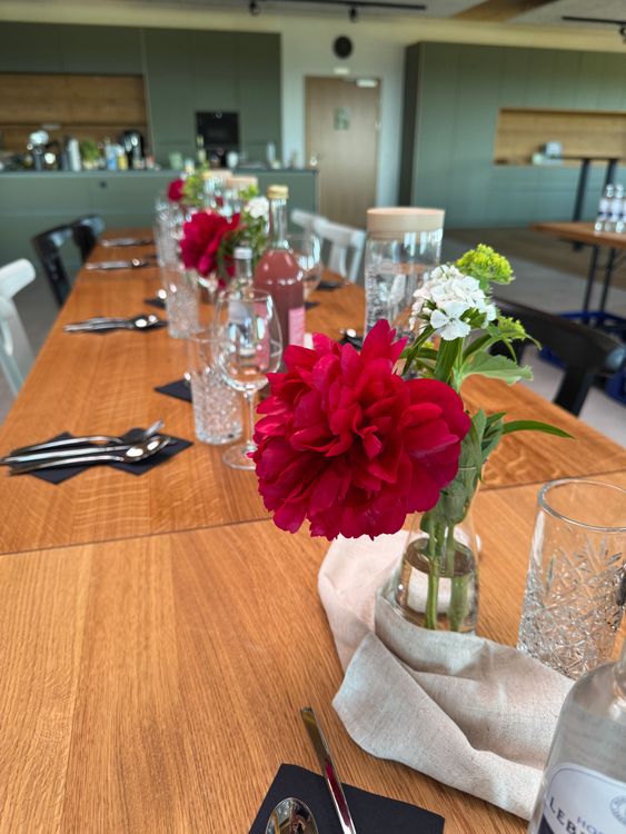 Tisch mit roten Blumen, Gläsern, Besteck und Flaschen in modern eingerichteter Küche