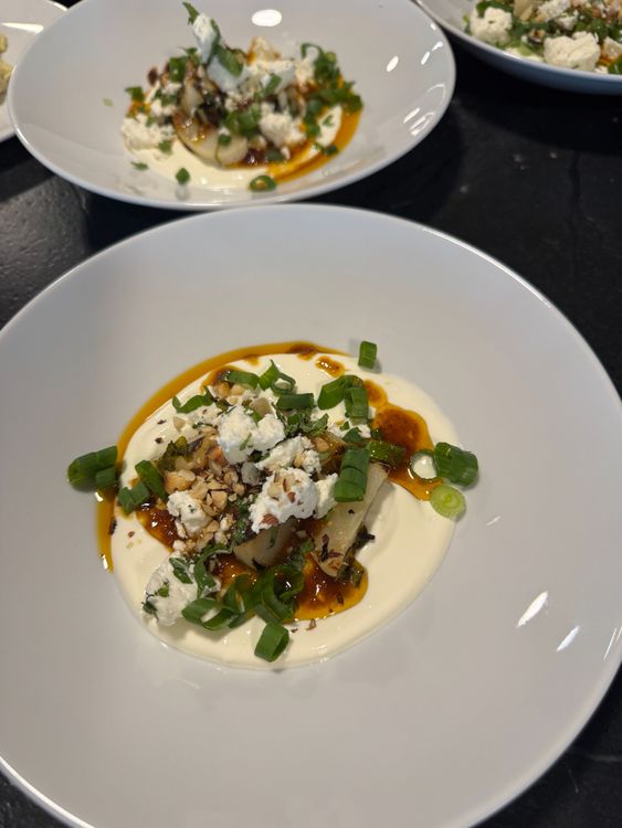Angerichtetes Gericht mit Joghurt, gehackten Nüssen, Frühlingszwiebeln, Feta und einer scharfen Soße in weißem Teller