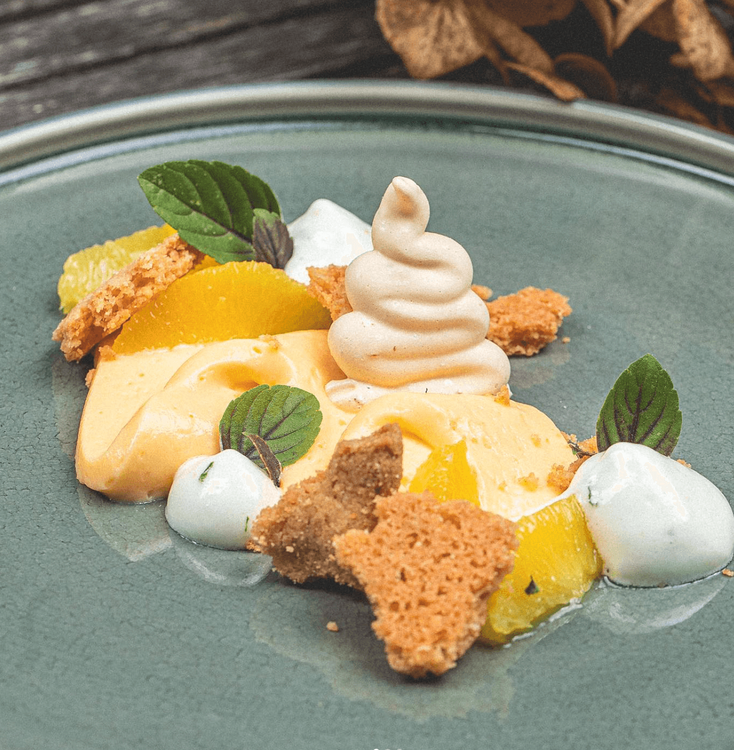 Kunstvoll angerichtetes Dessert mit Orangen, Creme, Minzblättern und Kekssternen auf grünem Teller
