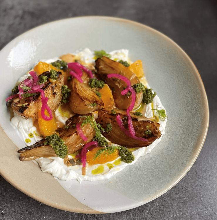 Gegrillter Fenchel mit Joghurt, Orangenstücken, grüner Sauce und eingelegten roten Zwiebeln auf einem Teller